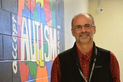 Sean Madden, special education teacher at New London High School, stands outside his student classroom. In the background is a piece of art from one of his former students.
