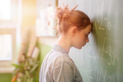 Student leaning head in frustration on classroom blackboard.