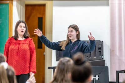 Cara Bernard looks on while Katie Cummins leads her music class.