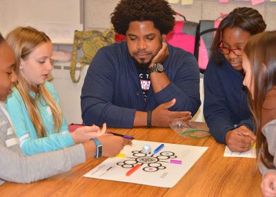 Black male teacher interacts with middle school students.