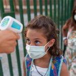 Little girl with face mask gets temp checked.