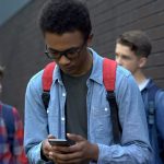 African American male teen looks at cellphone, fellow teens are in the back.
