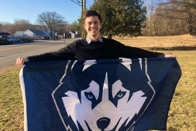 Class of 2021 senior Rowan Page smiles and holds up UConn Husky banner.