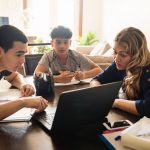 Mother and teenage sons gather around laptop to learn remotely.