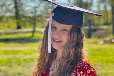 D'Lanie Pelletier stands outside smiling and wearing her 2021 graduation cap.