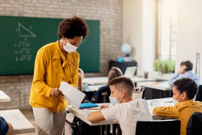 African American teacher works with school aged children, all are wearing masks.