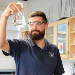 Mike Fenn in a science classroom holding a beaker.