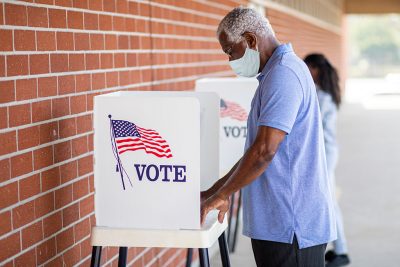 African American male with mask at voting booth.