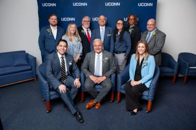 Group of professionals at gather in front of a UConn banner.