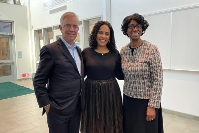 Two women of color stand with man in a suit.