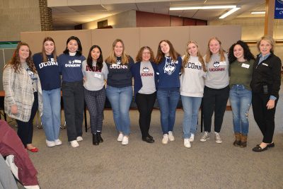 Smiling educators wearing UConn gear gather at a schoo.