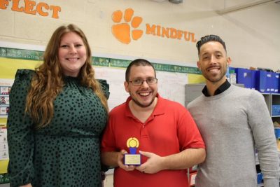 Three smiling educators, one holds award.