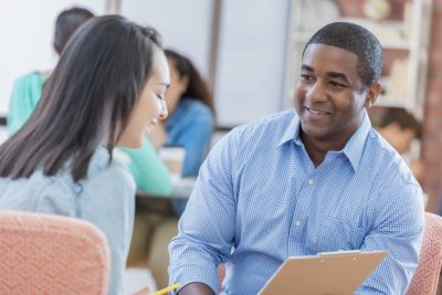 Mid adult African American school counselor talks with female student in the student lounge.