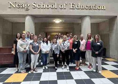 Group of educators stand in front of the Neag School sign. 