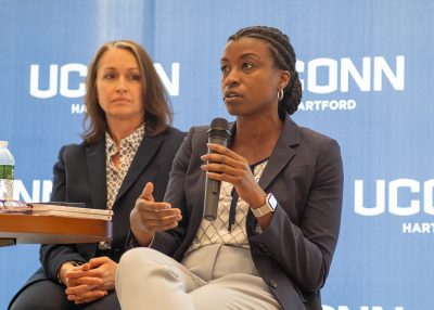 Two professional women speak in a panel in front of a blue banner.