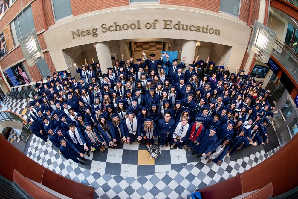 Neag School Class of 2023 graduates pose together in the Gentry Building atrium under the Neag School of Education lettering. [Links to UConn Today website]