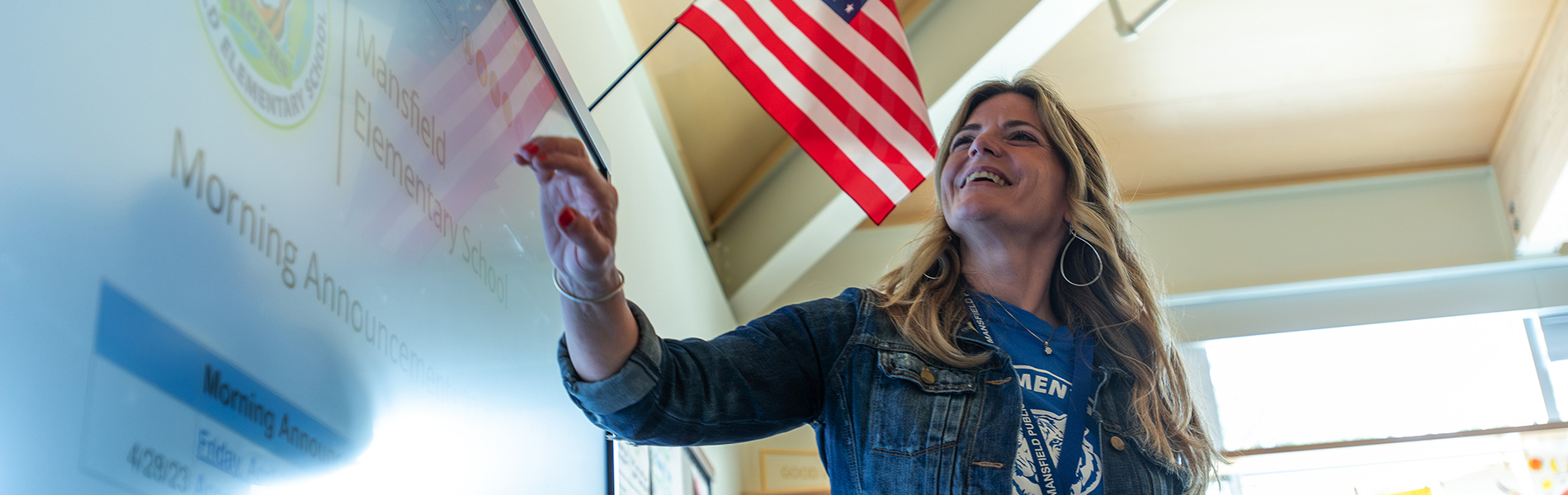 A white female teacher stands at a smartboard in a classroom.