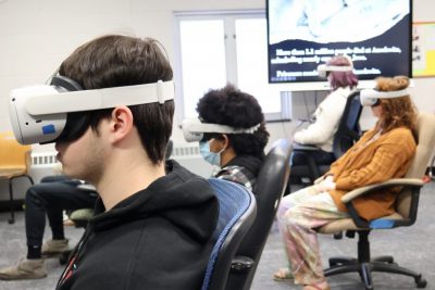 High school students wear virtual headgear in a classroom.