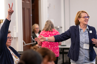 Female professional at a workshop, one has hand raised.