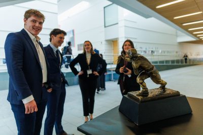 Four college students stand next to the Heisman Trophy.
