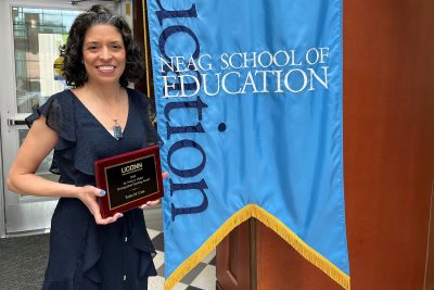 Tutita Casa holds an award plaque in front of the Neag School banner.
